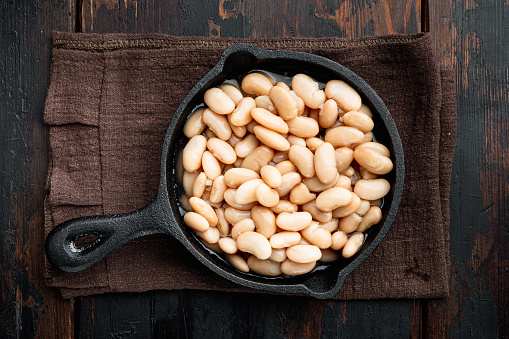 White canned beans set, in cast iron frying pan, on old dark  wooden table background, top view flat lay