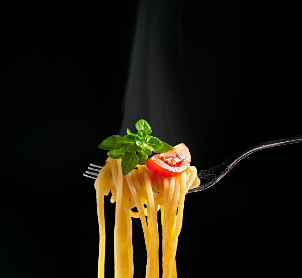 istock Fork with spaghetti, tomato and basil isolated on a black background. Hot spaghetti with steam 1314820376
