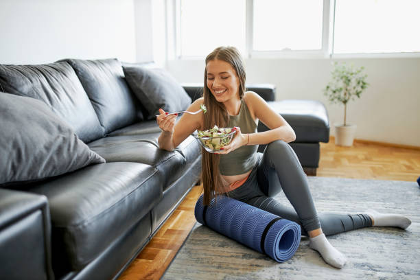 belle femme mangeant la salade fraîche après l’entraînement intensif à la maison - vegetarians photos et images de collection