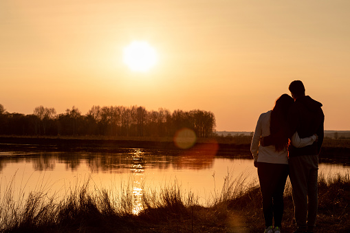 A young couple of lovers stands on the background of a sunny sunset near the river.