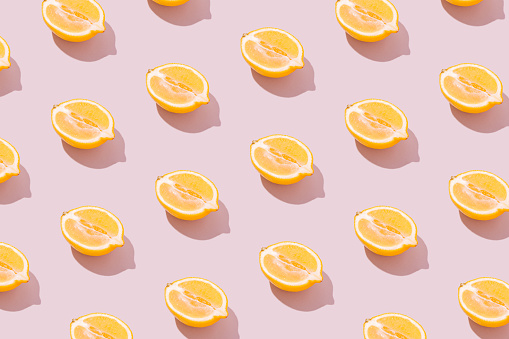 Lemon halves pattern on a pale pink background. Sunny yellow summer citrus fruit and shadow. Retro beach food aesthetic concept.