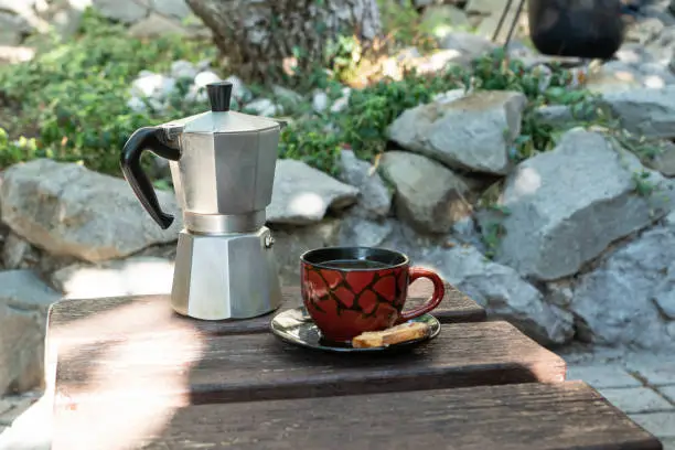 Outdoor summer breakfast with cup of coffee made with geyser coffeemaker and cookie stand on old wooden table in summer garden. Leisure and recreational concept