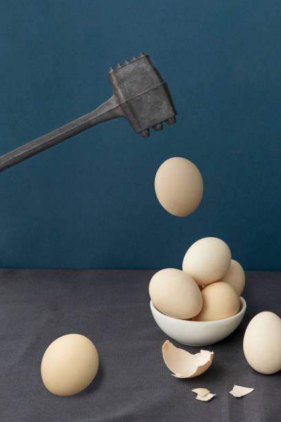 istock Iron hammer is about to hit flying levitating egg, other eggs lie in little round plate, dark blue background, copyspace. 1314823752