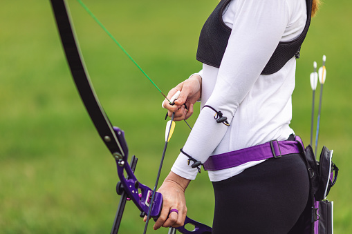 Woman practicing archery training with recurve bow on open field.