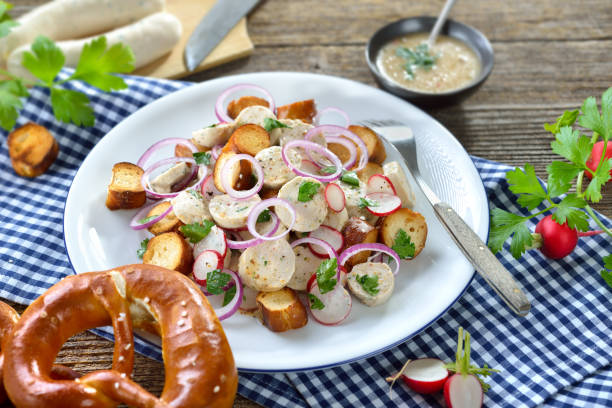 Bavarian cold summer salad with veal sausages Hearty Bavarian salad with cut veal sausages, roasted pretzel slices and a mustard dressing on a rustic wooden table weisswurst photos stock pictures, royalty-free photos & images
