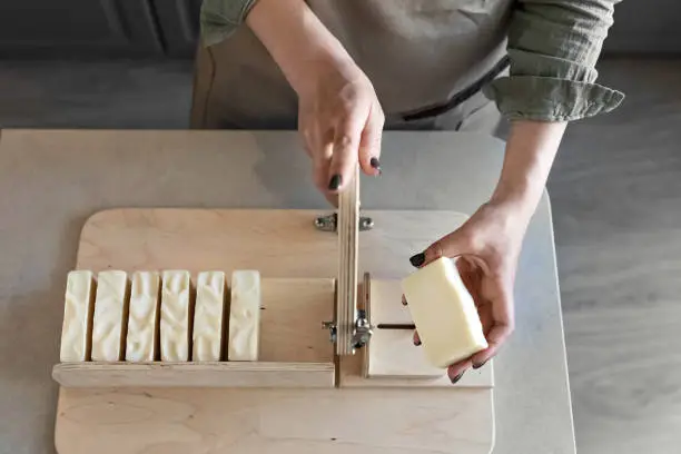 A woman makes handmade natural soap.The finished soap is cut into pieces using special machine. Home spa. Small business.