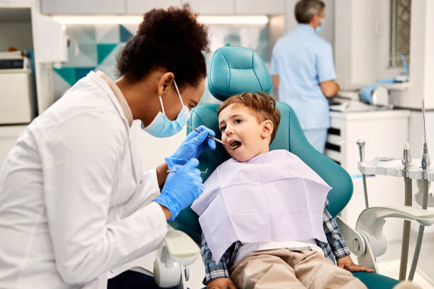 Little boy getting his teeth checked by dentist at dental clinic. Black female dentist examining small boy's teeth during dental procedure at dentist's office. Focus is on boy. dental hygienist stock pictures, royalty-free photos & images