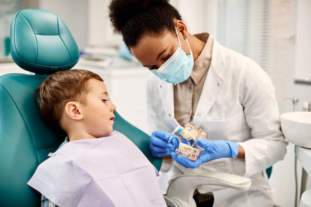 African American dentist teaching small boy how to brush teeth properly during dental appointment. Small boy sitting in dentist's chair and learning how to brush teeth properly. dentist photos stock pictures, royalty-free photos & images