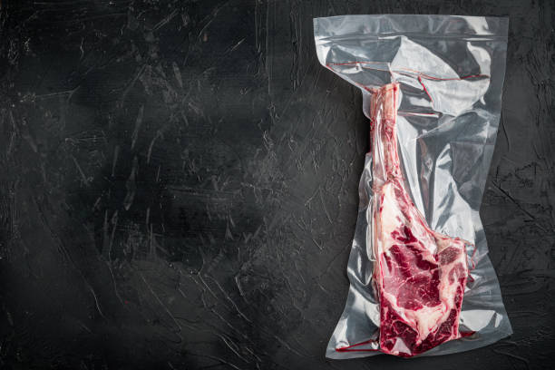 Bone Tomahawk Steak in vacuum commercial pack, on black stone background, top view flat lay, with copy space for text Bone Tomahawk Steak in vacuum commercial pack set, on black stone background, top view flat lay, with copy space for text vacuum packed stock pictures, royalty-free photos & images
