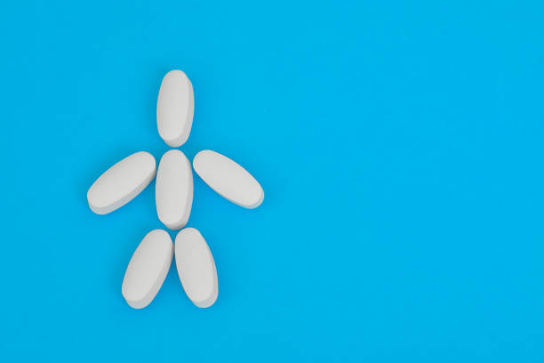istock Small human figure laid out from white oblong pills on blue background. Human skeleton. 1314843039