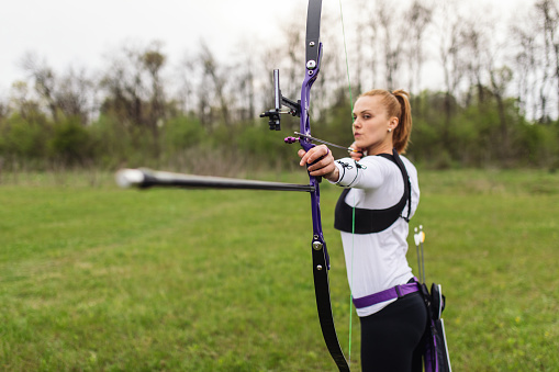 Woman practicing archery training with recurve bow on open field.