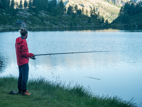 Dawn, young man fishing on weekend enjoying outdoor pursuit in remote location. Ticino, Switzerland