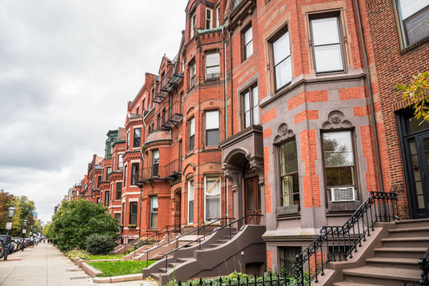 Row of traditional red-brick aprtment buildings and cloudy sky Row of old red-brick apartment buildings with staircases to the front doors along a tree lined street on a cloudy autumn day. Boston, MA, USA. row house stock pictures, royalty-free photos & images