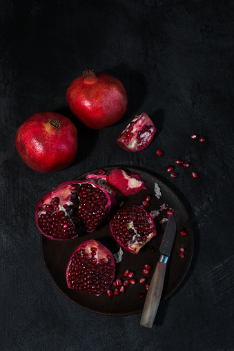 Stock photo showing a close-up view of healthy eating image of a wooden fruit bowl piled with  pomegranate (Punica granatum) seeds displaying red flesh (arils) encasing seeds on a red background.