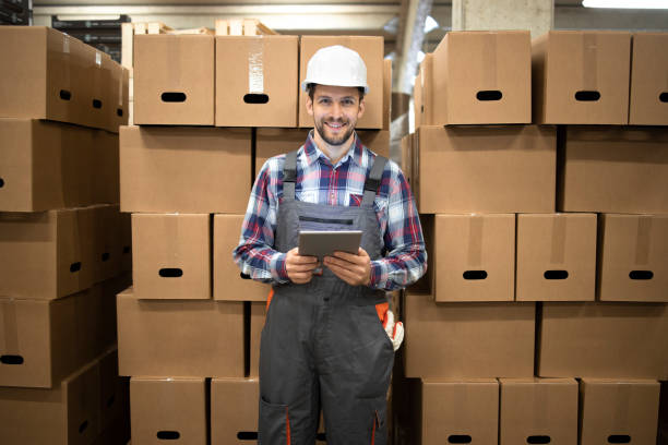 istock Portrait of warehouse supervisor holding tablet computer and standing by cardboard boxes with goods in factory storage room. 1314852162