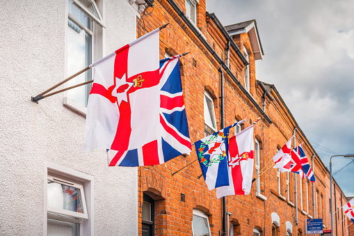 Flags of Northern Ireland, the United Kingdom and of the Ulster Scots on townhouses in Belfast, Northern Ireland, UK on a cloudy day.