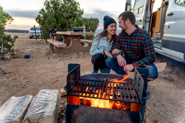 istock Young Couple Sitting By A Campfire Romantically Looking At Each Other Lovingly, Enjoying The Outdoors, Camping 1314864219