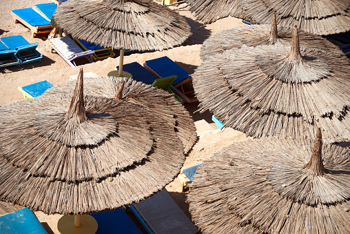 Straw beach umbrellas close-up abstract background, sun loungers and sand