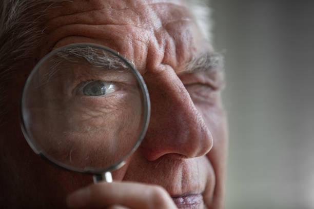 istock Close-up of Senior Man Looking at Camera Through Magnifying Glass 1314876566