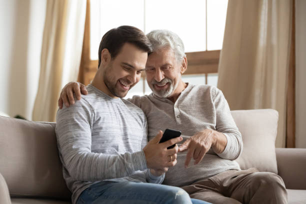 istock Smiling old dad and grownup son use cellphone 1314877570