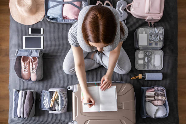 mujer turista sonriente empacando maleta a vacaciones escribiendo lista de papel preparándose para viajar viaje - empaquetar fotografías e imágenes de stock