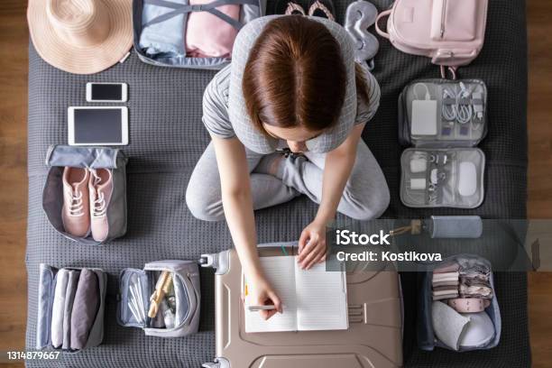 Smiling Tourist Woman Packing Suitcase To Vacation Writing Paper List Getting Ready To Travel Trip Stock Photo - Download Image Now