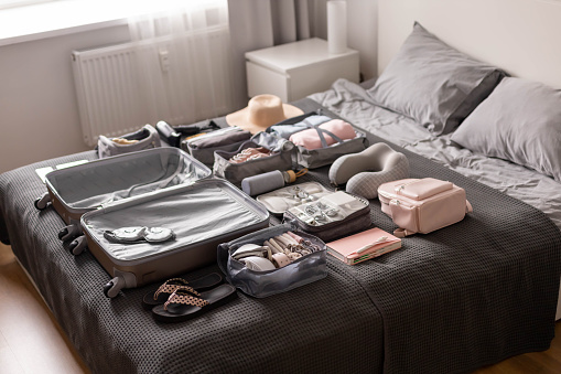 Woman at bedroom packing suitcase for vacation. She is using smart phone to check her reservation or to do list.