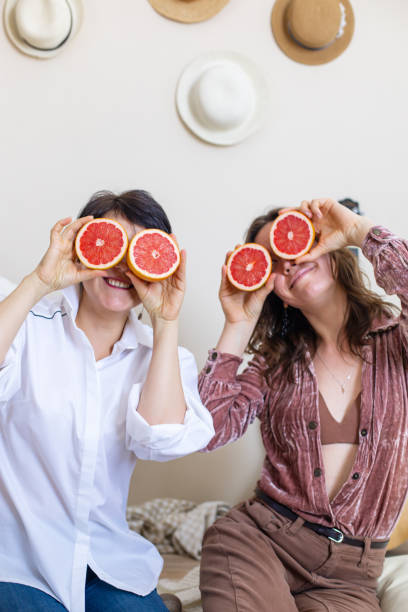 amigas felizes mostrando línguas posando com metades de toranjas nos olhos rindo de festa de galinha - vegan food cheerful vertical indoors - fotografias e filmes do acervo