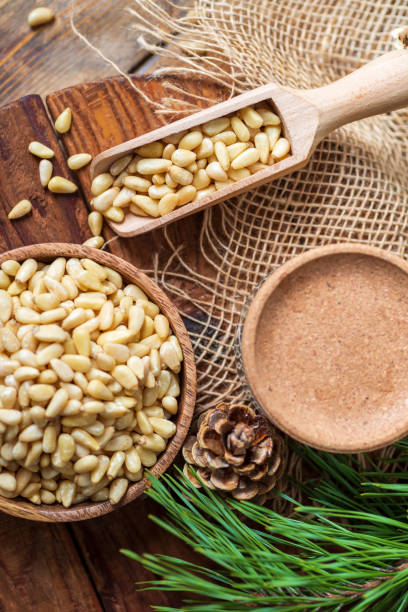 istock Peeled pine nuts in a bowl, pine cone on a cutting board, rough cloth next to it. View from above. Healthy food of forest gifts. 1314902678
