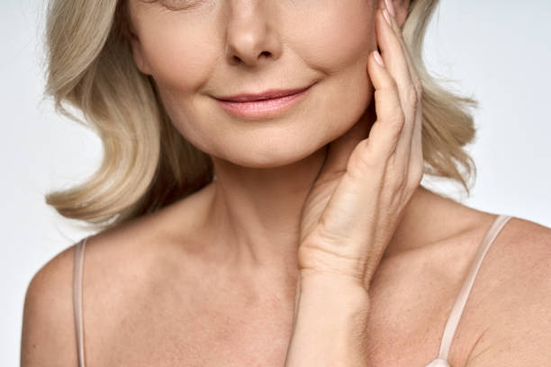 Face close up portrait of happy mid age 50 years old woman touching face with hand. Advertising of skin care anti wrinkle products for facial bottom part, lips, chin neck and decollete. Face close up portrait of happy mid age 50 years old woman touching face with hand. Advertising of skin care anti wrinkle products for facial bottom part, lips, chin neck and decollete. chin stock pictures, royalty-free photos & images