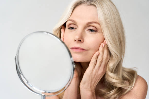 ritratto ravvicinato di una splendida donna felice di mezza età che guarda lo specchio che tocca la pelle godendosi il trattamento per la pelle secca. pubblicità di prodotti antiaging beauty per la cura della pelle. - bellezza foto e immagini stock