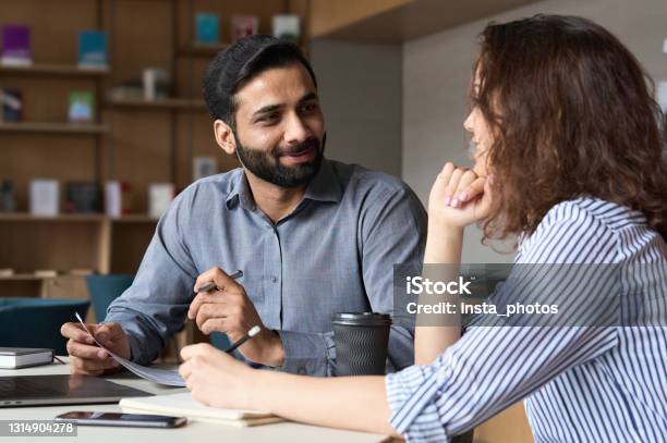 Interview Of Happy Smiling Indian Hr Manager With Latin Young Professional And Friendly Support Discussing Job Cv Mentoring Hispanic Male Teacher And Female Student In Multiethnic Creative Space Stock Photo - Download Image Now