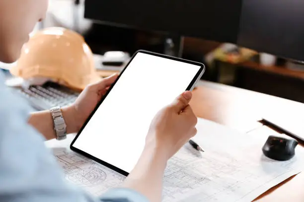 Photo of Architect reading building and  drawing outlay construction plan as guide for builders with details on tablet. Architecture, engineering, business and civil concept.