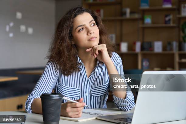 Young Indian Dreamy Thoughtful Student Looking Away Working On Laptop In Office Coworking Space Classroom Hispanic Student Using Computer For Remote Learning Online Training Stock Photo - Download Image Now