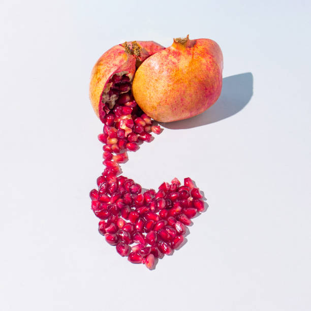 Creative composition with a freshly cut pomegranate makes a red heart on a gray background. Minimal fresh nature or love concept.