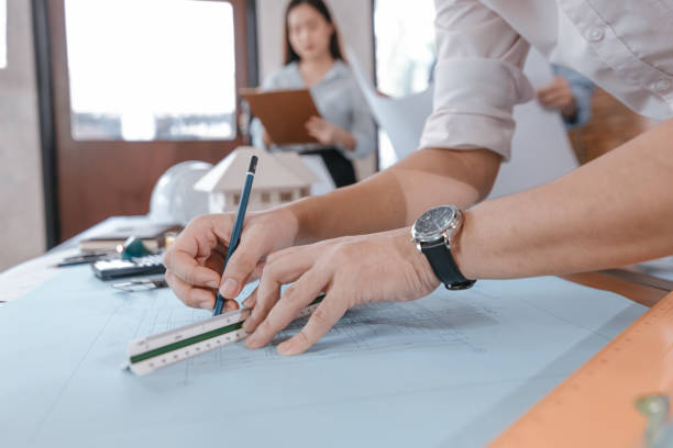 istock engineers holding a pen pointing to a building and  drawing outlay construction plan as guide for builders with details. Engineer design and writing blueprint. 1314905383