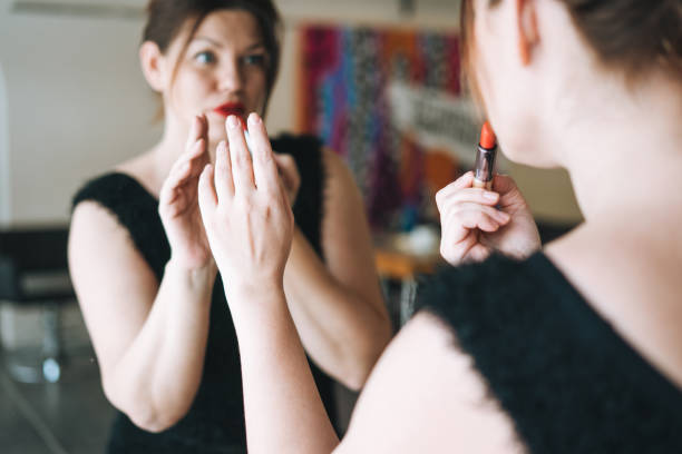 linda jovem sorridente plus size body positive em preto estilo de cabelo vestido de noite com batom vermelho nas mãos olhando para espelho em estúdio de beleza - big lips - fotografias e filmes do acervo