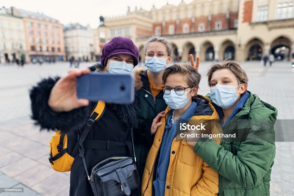Family sightseeing city during COVID-19 pandemic Family sightseeing city of Cracow, Poland on a sunny Spring day. During the COVID-19 pandemic everyone has to wear the surgical masks.
Family is making selfies in the main market square of Krakow.
Shot with Canon R5. Poland Stock Photo