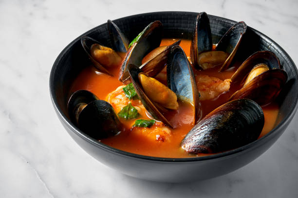 Thick Tuscan caciucco soup with seafood. Classic red soup with mussels, scallops and fish in a black plate on a marble background. stock photo