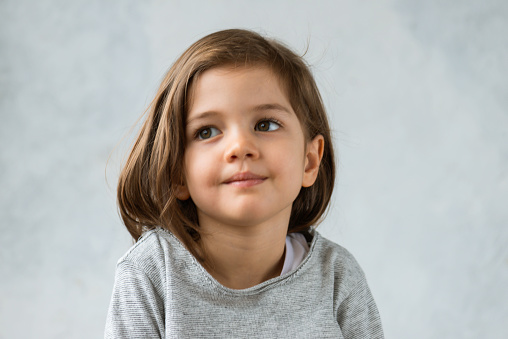 Toddler with a cute smile is looking up and daydreaming in front of blue gray wall.