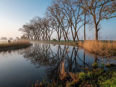Vroeg in de ochtend is een fietser op weg naar werk rijdend langs het riviertje de Vecht in de Nederlandse provincie Noord-Holland