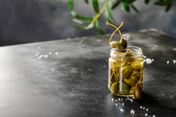 istock Capers. Marinated or pickled canned capers fruit close up in glass jar on gray kitchen table background. Copy space 1314916361
