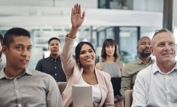 foto de una joven empresaria levantando la mano durante una presentación en una oficina - seminar asking business meeting fotografías e imágenes de stock