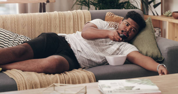 Shot of a young man lying on his couch at home Finally my favourite TV show is on laziness stock pictures, royalty-free photos & images