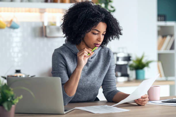 istock Afro business woman working with computer while consulting some invoices and documents in the kitchen at home. 1314926450