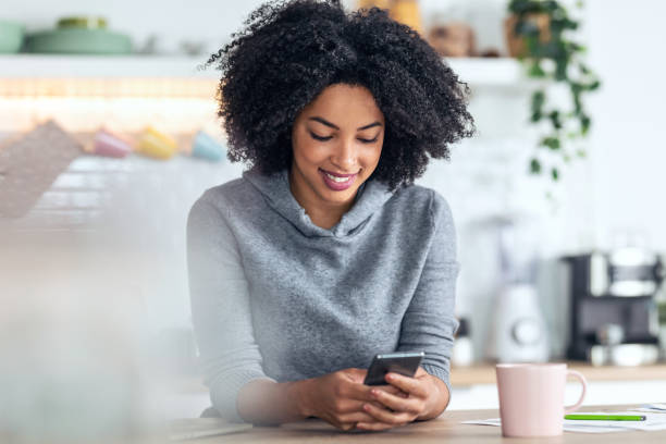 istock Beautiful afro business woman talking with her mobile phone while working with computer in the kitchen at home. 1314926910