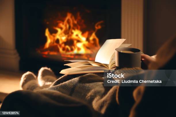 Woman With Cup Of Drink And Book Near Fireplace At Home Closeup Stock Photo - Download Image Now