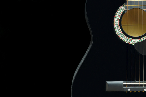 Black acoustic guitar on a black background. Free space for an inscription. Copper yellow strings