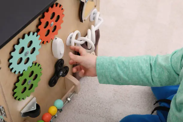 Photo of Little child playing with busy board house on floor, closeup