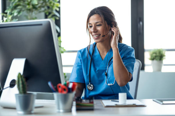 Female doctor talking with earphone while explaining medical treatment to patient through a video call with computer in the consultation. Shot of female doctor talking with earphone while explaining medical treatment to patient through a video call with computer in the consultation. using phone stock pictures, royalty-free photos & images